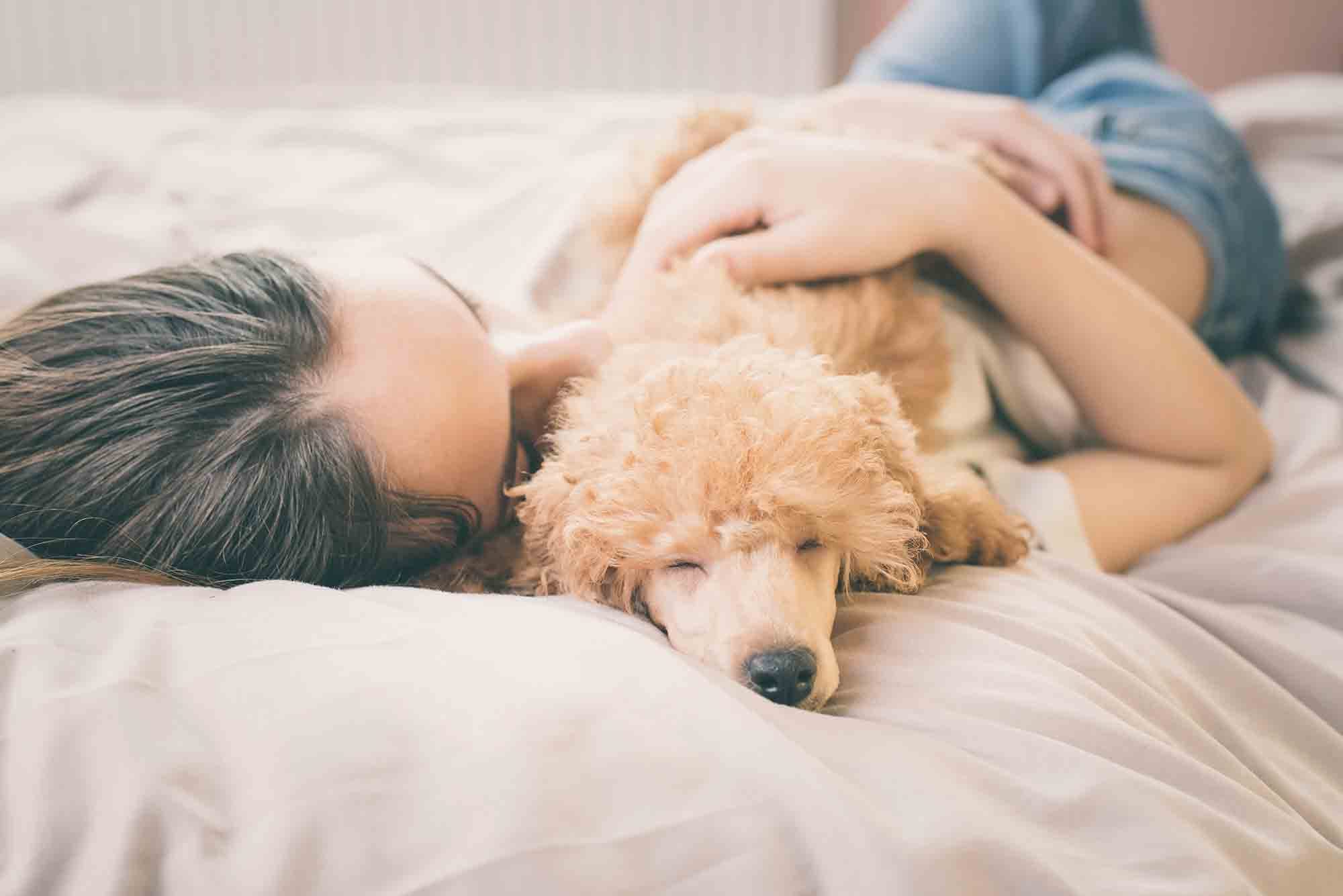 Young woman laying on bed snuggling with her dog